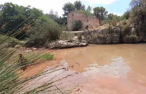 The main pool at Fuente de Marzo is a brown-pink colour, with an old building in the background