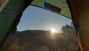 The sunrise is peeking out from behind the mountain opposite, viewed from inside of a tent