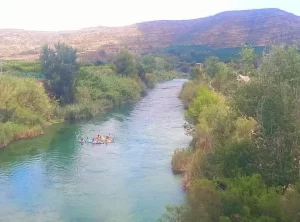 A group of people are rafting on the Júcar river with beautiful scenery in the background