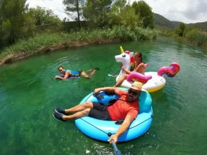 Three people are white water rafting, using an inflatable unicorn, bodyboard and rubber ring as their rafts